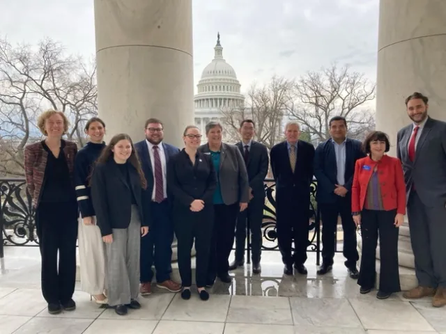 Group of people stand with U.S. capitol in the background.