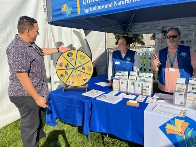 Two smiling Master Gardeners wearing vests help someone answer questions.
