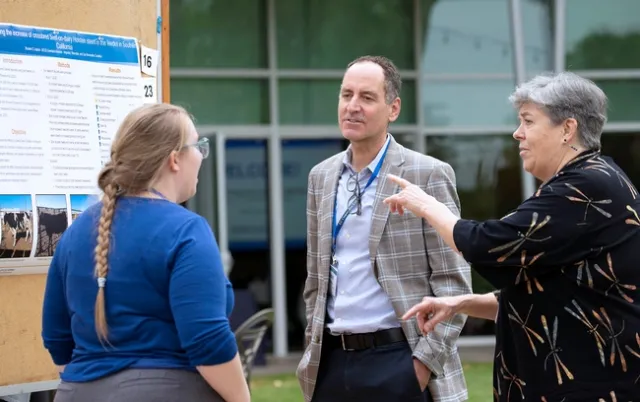 A man and woman speak with a young lady about her research.