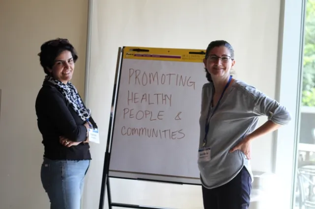 Two women standing in front of a poster smile at the camera.