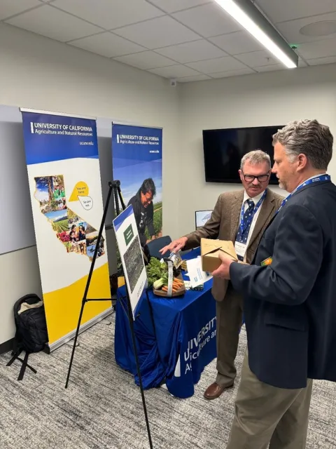 Steve gestures toward a photo of the machine as he speaks to a man in a suit holding a box of lunch leftovers.