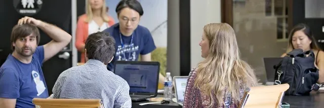 A group of employees are gathered around a table in a collaborative setting.