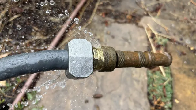 A hose with water spraying out where it’s connected to the nozzle.