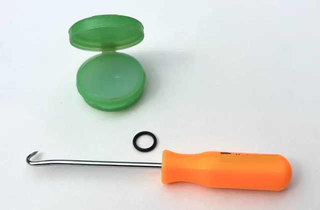 A pick tool with a sharp point, a small container of silicone grease, and an O-ring.