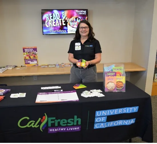 Lori stands behind a table displaying CalFresh Healthy Living University of California recipes and other handouts