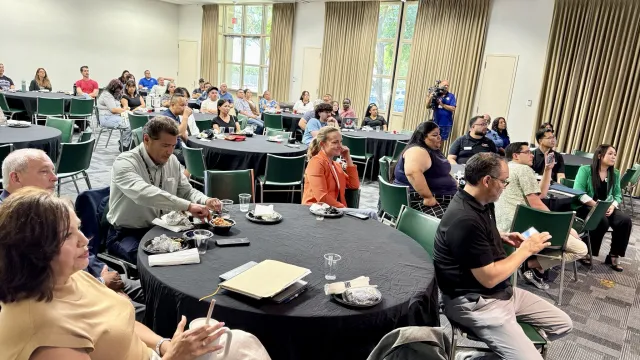 Dozens of people sit at tables watching a speaker