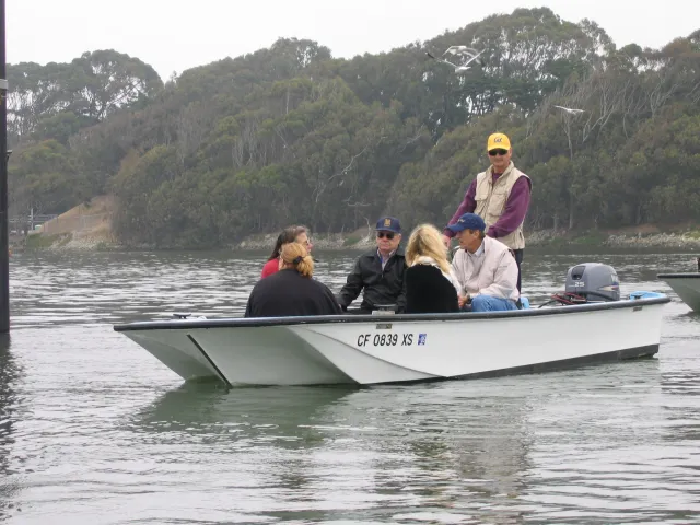 Five people seated and one standing in boat