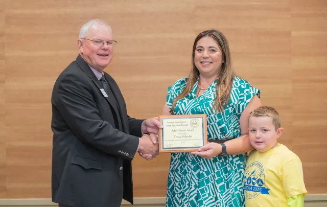 Man in dark suit hands Tracy Schohr a plaque