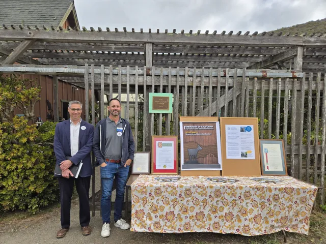Igor and Darren stand beside a table displaying the framed proclamation.