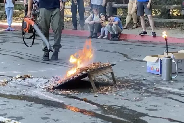Leafblower simulates wind fanning flames as people watch it burn