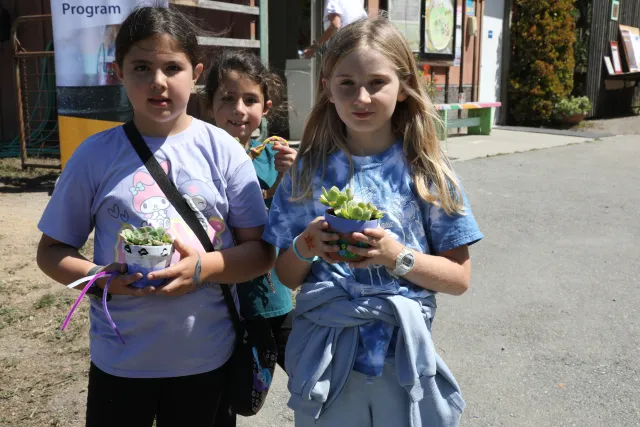 Three kids each hold a pot containing a succulent plant
