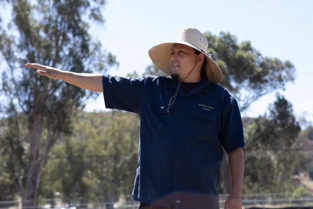 A person wearing a hat gestures to his outdoor surroundings