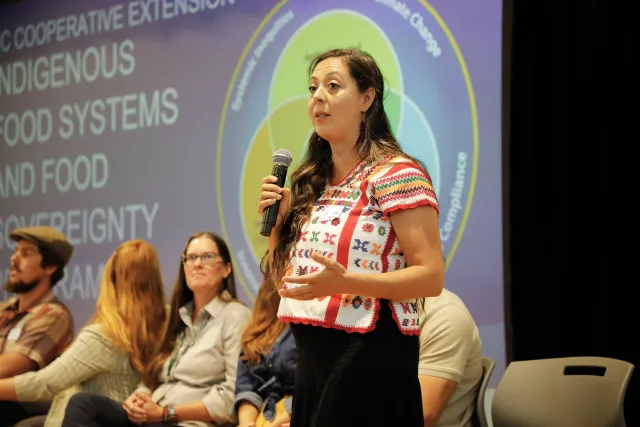 A person on stage speaks to an audience