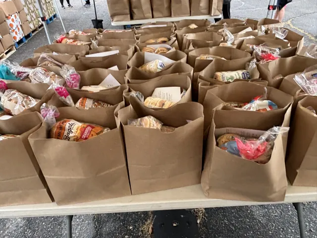 Grocery bags of food sit atop a table outside.