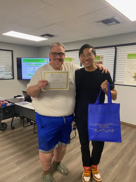 Bobby Burke holds his course completion certificate as he puts his arm around the shoulder of educator Danny Vang, who holds a UC nutrition education tote bag