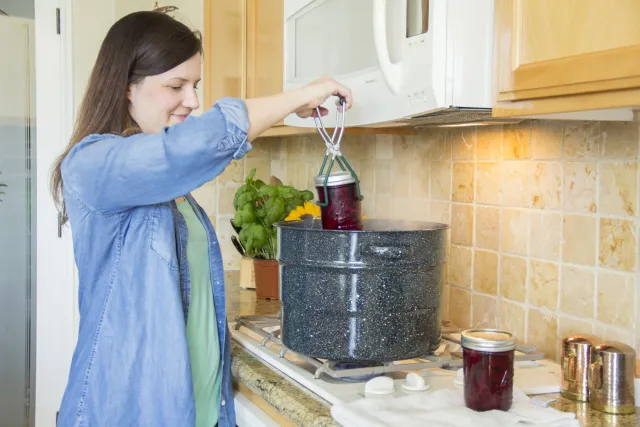 Woman lifting jar of pickled beets out of boiling water bath canner. 