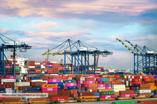 The Port of Los Angeles filled with brightly colored shipping containers and a container ship docked next to cranes.