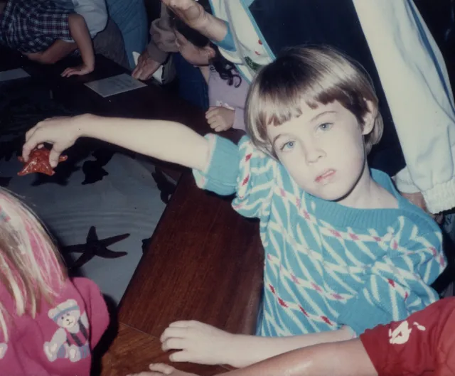 Young girl wearing a light blue-green sweater holds a sea star replica; the photo looks to be from the 1980s