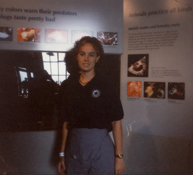 Teenage girl in a black polo shirt stands in front of an aquarium exhibit; photo appears to be from the 1990s
