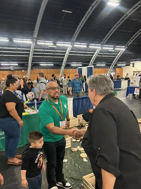 Glenda shakes hands with Diego Mariscal, who is standing beside a small boy.