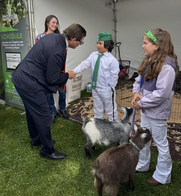 Jones shakes hands with young 4-H member holding the leash of a goat as Anne and another 4-H member look on
