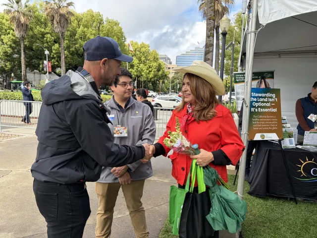 Darren Haver shakes hands with a woman wearing a red jacket and cowboy hat as Nestor looks at her