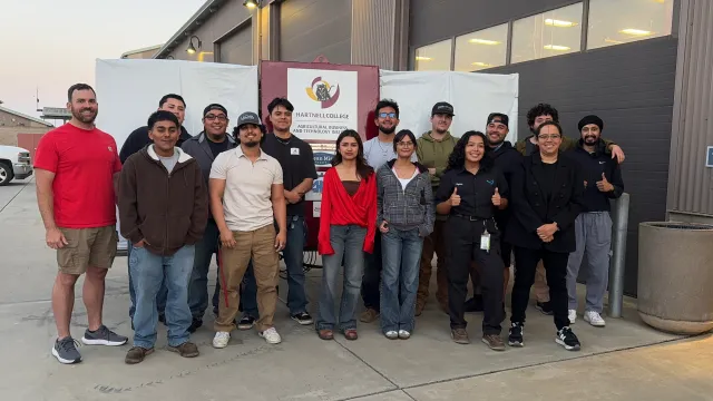 Red Scout team of Hartnell College pose by a Hartnell sign outside a building