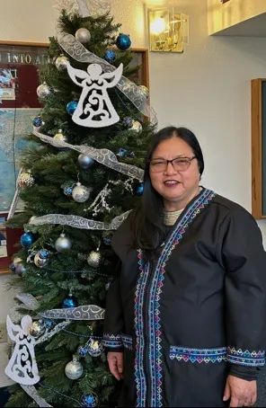 Fam Lee dressed in traditional Iu Mien clothes, standing by a Christmas tree