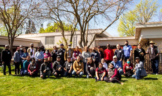 Hmong and Iu Mien farmers gather with UCCE personnel at an annual meeting, lined up in rows for a group photo on a lawn and under a tree