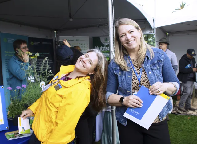 Lauren Snowden, leaning back, and Missy Gable pose in front of potted plants at their booth