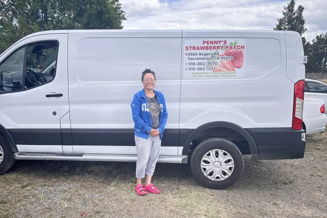 Iu Mien farmer Penny poses by her white van that says "Penny's Strawberry Patch"