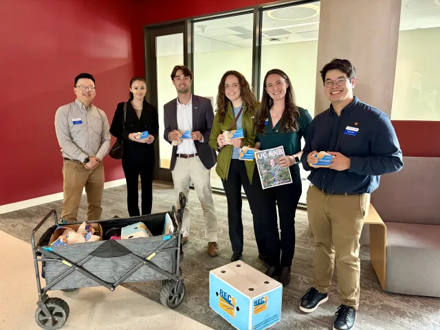 Six people stand in a row, five of them holding small bags of citrus with postcards attached