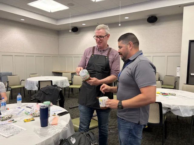 Two men stand looking at their coffee mugs