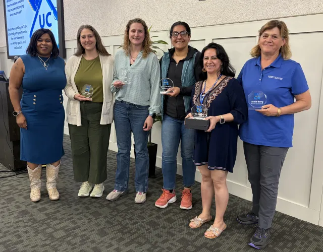 Six women stand in a row. Five of them are holding lucite trophies