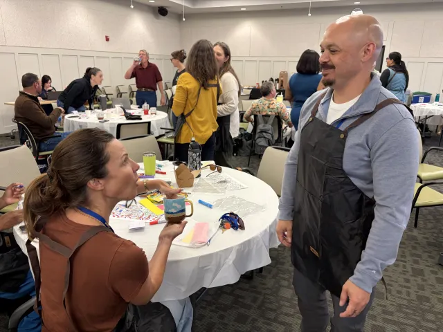 A woman sitting at a round table speaks with a man who is standing