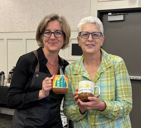 Two women hold up decorated mugs