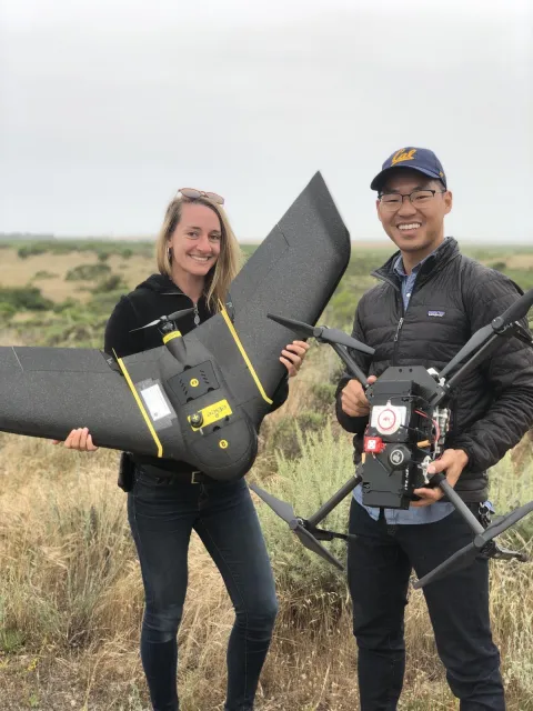 Two people smile at the camera holding drones