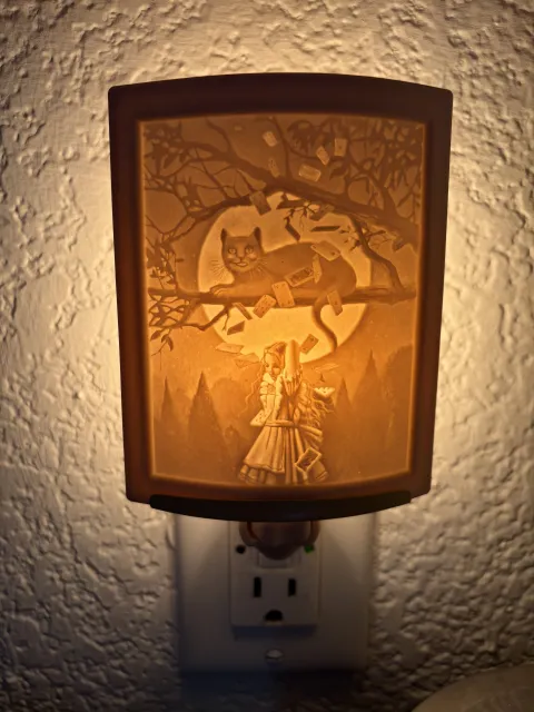 A glowing nightlight of a grinning cat perched in a tree over Alice, who is standing below. Playing cards are falling from the tree