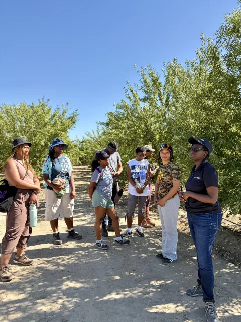 Standing in the shade of an orchard, Jackie speaks to a group of students