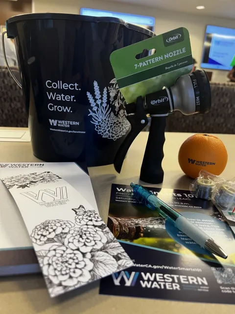 A bucket, spray gun for a water hose, pen, and handouts on a table.
