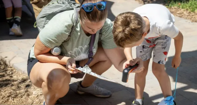 Adult and child participate with a handheld device in an activity during the Celebration of Cool Event