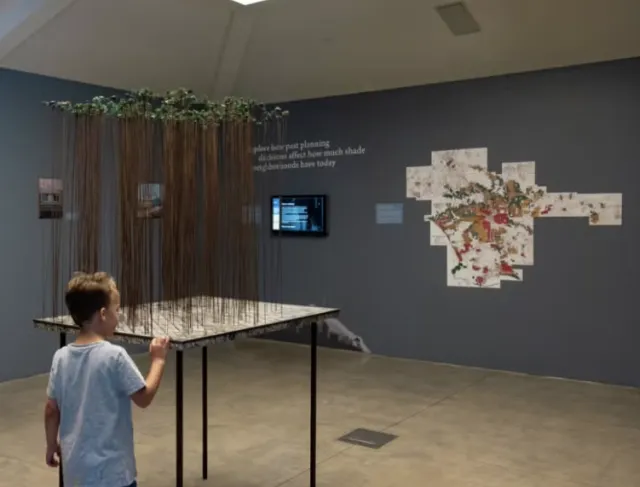 A child views an exhibit on a table of "trees" made of wire trunks with little green leaves on top