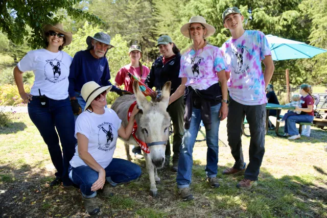 Seven people pose with a donkey who is wearing a party hat and red sash
