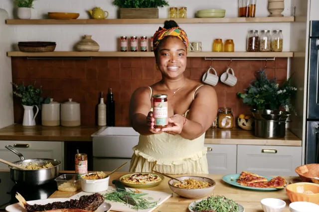 Woman standing in a kitchen holds up a jar of chili oil
