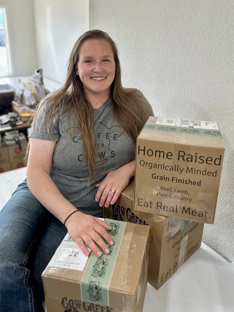 Kelsey Arreche poses by boxes of products from Cow Creek Meat
