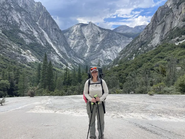 Kristin Polidoro stands with hiking poles, with Kings Canyon behind her and the South Fork of the Kings River below, unseen