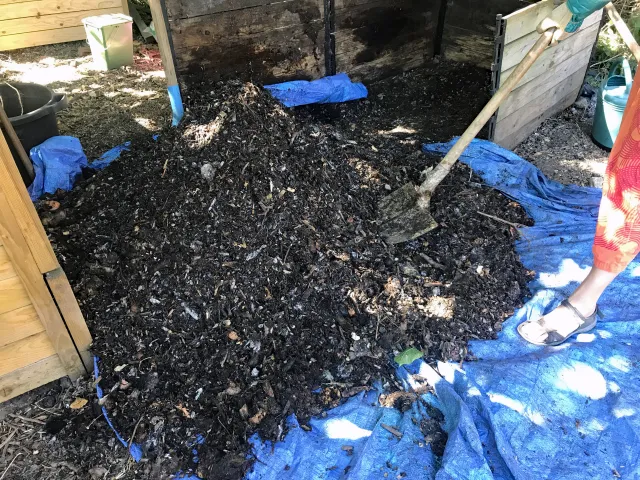 Person using a shovel to turn compost pile.