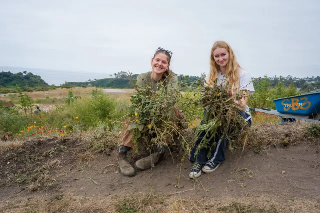 Katja Reinwald (left) and Eliza Emery hold up the invasive weeds they pulled up during a Climate Stewards activity