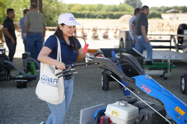 A person poses, holding onto the handles of a small tractor