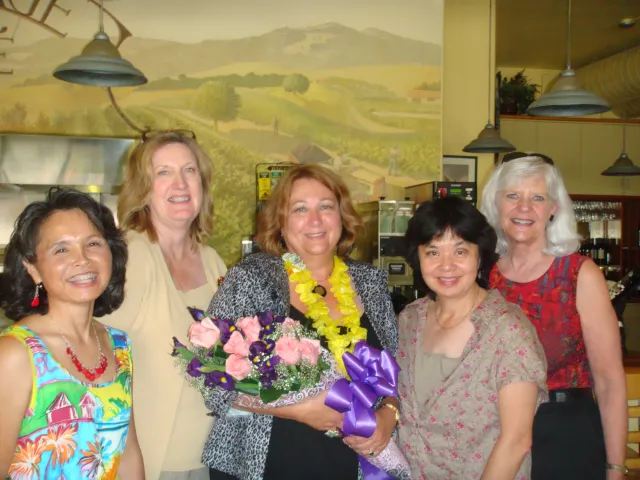 Five women. Woman in center is holding a bouquet of flowers